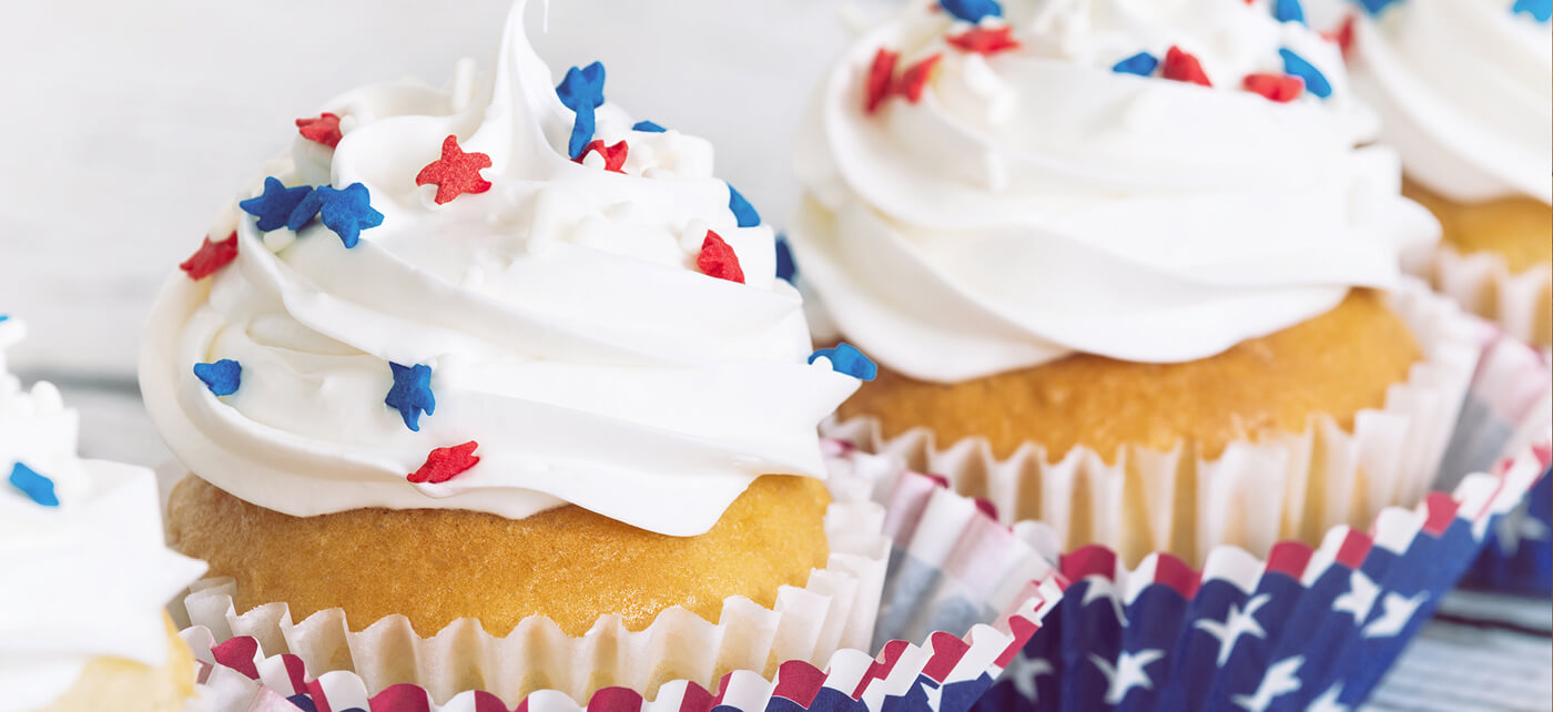 Close-up of vanilla cupcakes topped with white buttercream and red and blue star sprinkles in festive liners