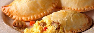 Golden-brown breakfast empanadas with crimped edges, with one cut open to reveal a filling of scrambled eggs, sausage, and peppers.