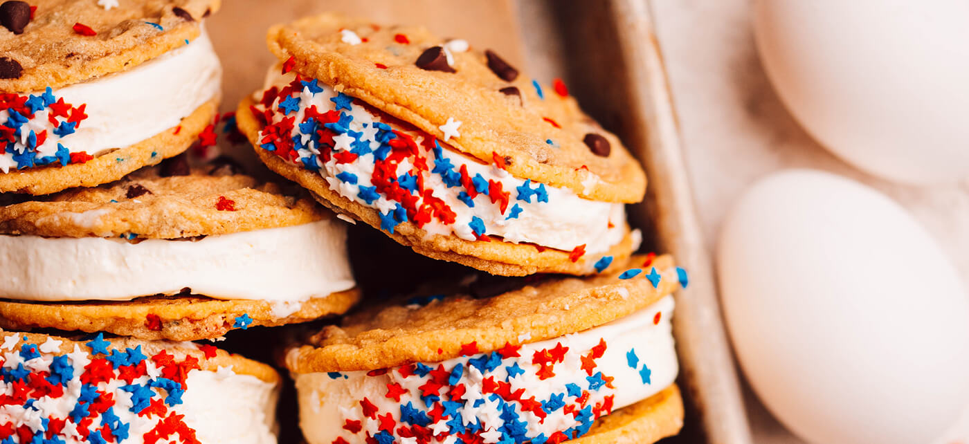 Stacked ice cream sandwiches with vanilla filling rolled in patriotic star sprinkles between golden cookies