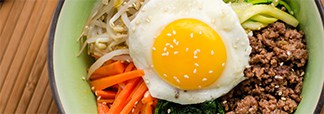 A bibimbap bowl topped with a sunny-side-up egg, seasoned ground beef, julienned carrots, bean sprouts, and greens, sprinkled with sesame seeds.